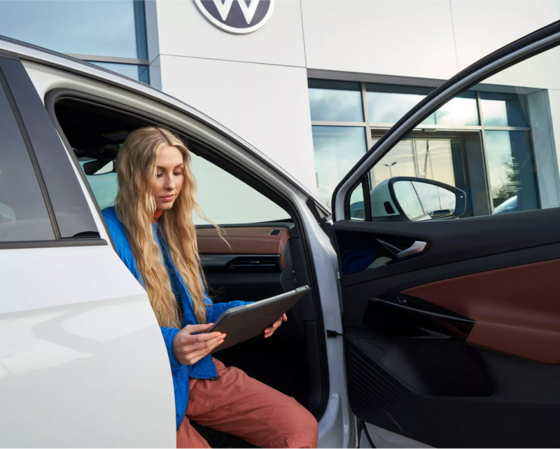 Mujer sentada en un vehículo VW revisando el reporte de cobertura sin preocupaciones.