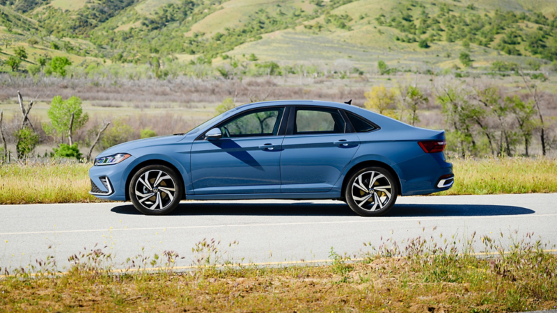 Side view of the blue 2025 VW Jetta parked on a scenic road with hills and greenery in the background. 