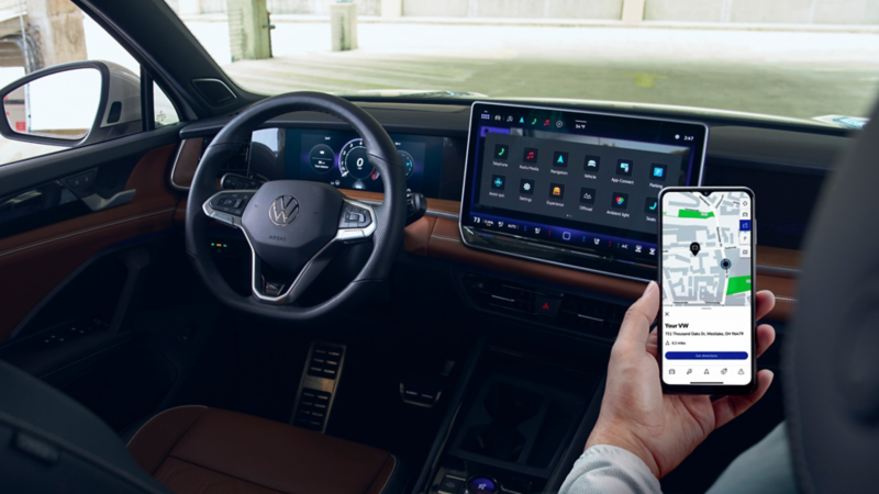 The front passenger in a parked Tiguan holds a smartphone in front of the center touchscreen display.