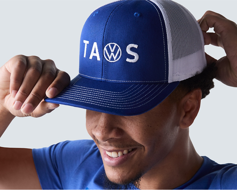 man in the foreground smiling as he shows off his blue VW cap
